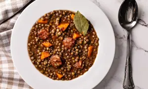 Un plato de lentejas estofadas con trozos de zanahoria y chorizo, decorado con una hoja de laurel.