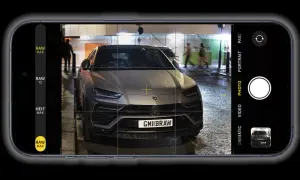 Un'auto sportiva grigia, con targa GMIIBRAW, inquadrata dall'app fotocamera di un iPhone con opzione apple proraw attiva.
