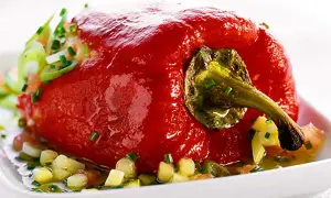 En fylld, röd paprika serveras på en vit tallrik med en sallad av tärnad paprika och örter. Ett läckert recept med grillad paprika på burk.