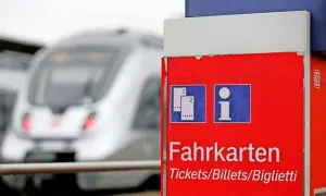 Roter Fahrkartenautomat am Bahnhof. Ein Zug fährt vorbei. Wann am besten Bahntickets buchen? Hier gibt es Infos.