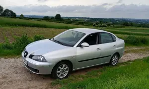 Srebrny Seat Cordoba na tle zielonych pól i pagórków.