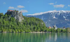 Blick auf die Burg von Bled über dem smaragdgrünen See, mit schneebedeckten Bergen im Hintergrund.
