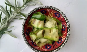 Gegrillte Zucchinibänder in einer bunten Schale mit Rosmarinzweig.