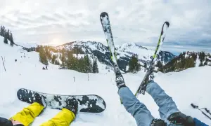 Narciarz i snowboardzista odpoczywają na stoku. Zastanawiasz się, co bardziej obciąża kolana: narty czy snowboard? Góry i słońce zachęcają do jazdy.