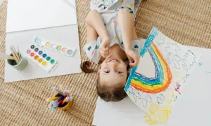 Niña sonriente haciendo un arcoíris, rodeada de acuarelas y rotuladores. Perfectas actividades de verano para niños creativos.