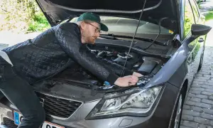 Man med keps och glasögon böjer sig över motorhuven för att byta halogenlampa.