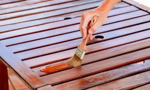 Mano aplicando barniz a una mesa de madera. Se puede barnizar sin tapaporos para un acabado rápido y protector.