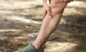 Uomo con mano sulla tibia, avvertendo dolore tibiale anteriore a riposo. Scarpa da ginnastica verde in primo piano.