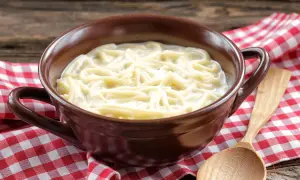 Eine Schüssel mit milch nudeln, serviert auf kariertem Stoff. Ein Holzlöffel liegt daneben.
