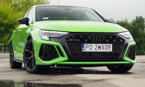 Jaskrawozielone Audi RS3 Sedan z czarnymi felgami stoi na mokrej nawierzchni, odbijając się w kałużach.