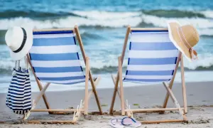 Dwa leżaki plażowe z niebiesko-białymi pasami, kapelusze i torba na piasku, z widokiem na morze.