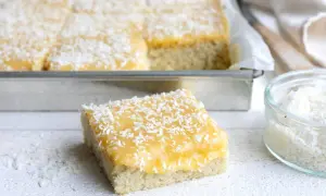 En bit av en saftig silviakaka i långpanna, toppad med gul glasyr och kokosflingor.