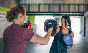 Due donne si allenano nel **boxing** in palestra. Una tiene i guantoni da allenamento, l'altra indossa un guantone blu.