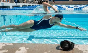 A swimmer performs the combat sidestroke in a pool, with a smartwatch on their wrist tracking their progress.