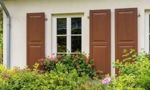 Okna drewniane z brązowymi okiennicami i kwitnącymi pelargoniami. Klasyczny urok, który przemawia za drewnianymi oknami.