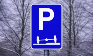 Blå parkeringsskylt med vitt P och en bild av en axel med hjul på en ramp. Förståelse av parkeringsskyltar är viktigt för att veta var man får parkera.