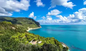 Vista mozzafiato dal belvedere Monte Conero: mare azzurro, costa verdeggiante e nuvole bianche nel cielo.