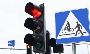 Sygnalizacja świetlna pokazuje czerwone światło, a obok znak informuje o przejściu dla pieszych i rowerzystów. Nie ryzykuj przejazdu na czerwonym świetle!