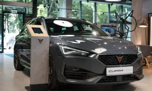 Szary Cupra Leon w salonie, gotowy do pokazania swojej mocy silnika. Obok stoi ekran informacyjny.