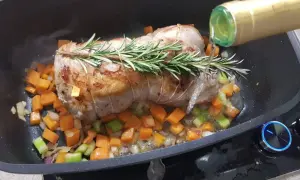 Arrosto di vitello in pentola con verdure e rosmarino, mentre viene sfumato con vino bianco.