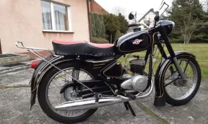 Czarny motocykl WSK z czerwoną kanapą i złotymi ozdobami, stojący na podjeździe.