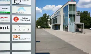 Tablica z nazwami firm, w tym "BiG Biuro Rachunkowe", przed nowoczesnym budynkiem biurowym.