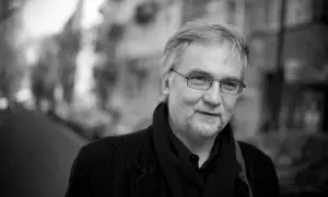 Portret Jerzego Pilcha w okularach, w czarnym sztruksowym płaszczu i szaliku.