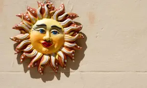 Sole decorativo in ceramica, un esempio di artigianato italiano, con volto sorridente e raggi colorati su muro beige.
