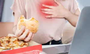 Osoba z bólem w klatce piersiowej trzyma gryzionego burgera. Obok pizza. Zastanawia się, co jeść na zgagę.