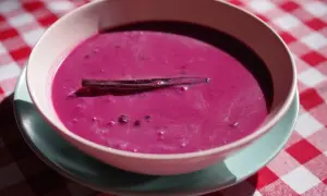 Aksamitna zupa jagodowa z laską wanilii, podana w miseczce na kraciastym obrusie.