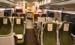 Wnętrze wagonu PKP Intercity z zielonymi siedzeniami i stolikami. Widoczny bar z pracownikiem. Rozkład miejsc IC 38172.