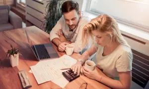 Couple calculant la refacturation de la taxe foncière pour un bail commercial, avec un ordinateur portable et des documents sur la table.