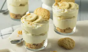 Warstwowy deser z bananów w szklankach, przełożony kremem i ciasteczkami.