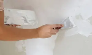 Manos aplicando masilla blanca en una pared con espátulas. La mejor masilla para paredes deja un acabado liso y perfecto.