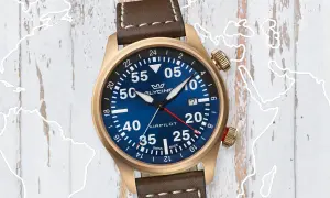 Zegarek lotniczy Glycine Airpilot z brązowym paskiem na tle mapy świata. Pozwala śledzić czas w różnych strefach, odpowiadając na pytanie, co to GMT.