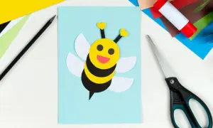 Ein süßes Biene basteln-Projekt auf hellblauem Papier. Bunte Bastelmaterialien, Schere und Klebestift liegen bereit.