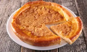 Une tarte au sucre dorée, avec une tranche coupée, sur une assiette blanche posée sur un fond en bois rustique.