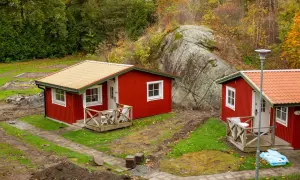 Dos casitas rojas de madera, ideales para un terreno. Rodeadas de naturaleza y una gran roca.