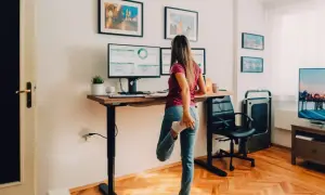Femme s'étirant à son bureau réglable en hauteur, profitant du confort au bureau avec ses deux écrans.