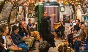 Artistas flamencos de Granada actúan en un tablao íntimo, con una bailaora en primer plano y un guitarrista acompañando.