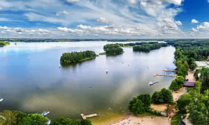 Malownicze zalewy w Polsce z żaglówkami, wyspami i plażą pełną wypoczywających ludzi.