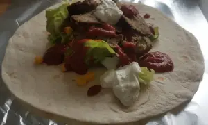 Domowy kebab z baraniną, sałatą, kukurydzą, sosem pomidorowym i jogurtowym na tortilli.