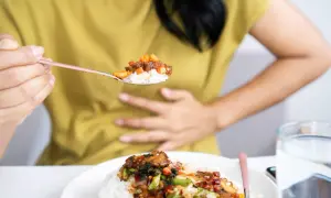 Persona con mano sull'addome, mangia riso piccante. Potrebbe soffrire di stitichezza.
