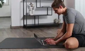 Mann auf Yogamatte tippt auf Laptop, um den Buckel wegtrainieren.