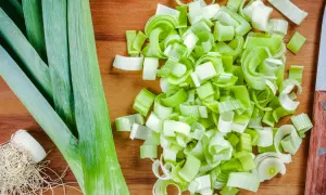 Frischer Lauch, bereit für leckere porree rezepte. Ganze Stangen und fein geschnittene Ringe liegen auf einem Holzbrett.