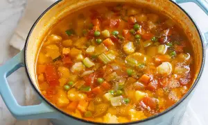 Un fumante minestrone di verdure in una casseruola blu, ricco di carote, zucchine, piselli e cavolfiore.