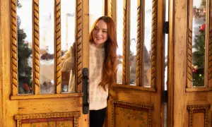Lindsay Lohan w świątecznym swetrze zagląda przez ozdobne drzwi. W tle choinka, jak w jej filmach.