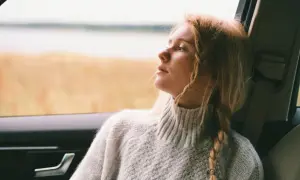 Ragazza con capelli biondi raccolti in acconciature trecce laterali, guarda fuori dal finestrino dell'auto, immersa nei suoi pensieri.