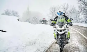 Motocyklista w kasku i zimowej odzieży jedzie po zaśnieżonej drodze.