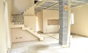 Wnętrze w trakcie budowy, schody i ściany pokryte tynkiem cienkowarstwowym wewnętrznym. Betonowy słup i sufit z widocznymi instalacjami.